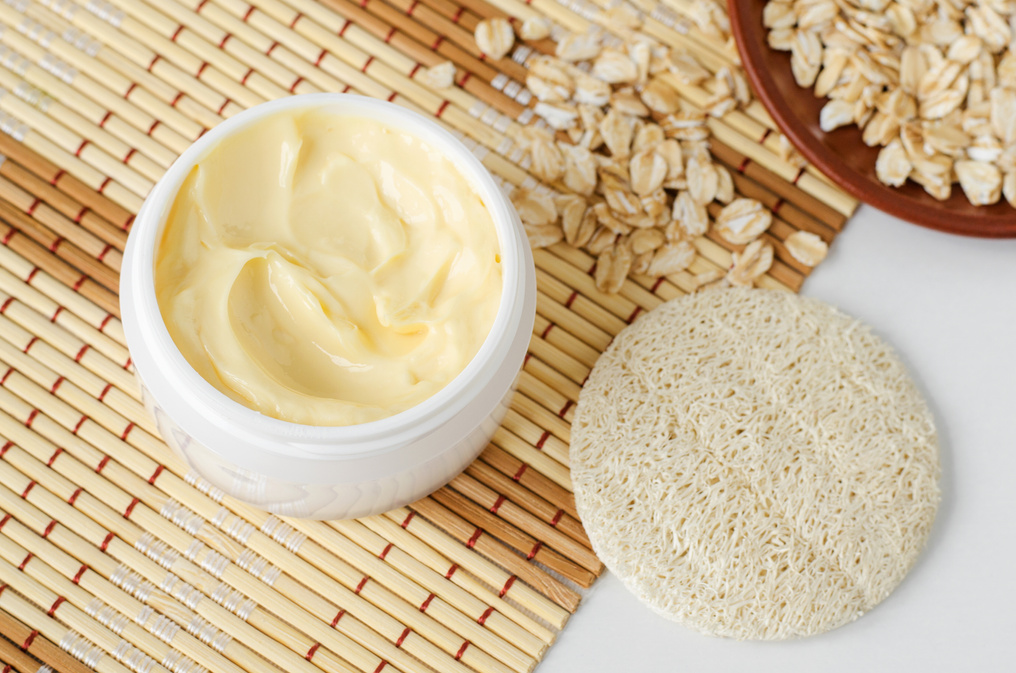 Yellow facial mask (oatmeal face cream, shea butter hair mask or body butter) in the small white jar. Natural skin and hair concept.